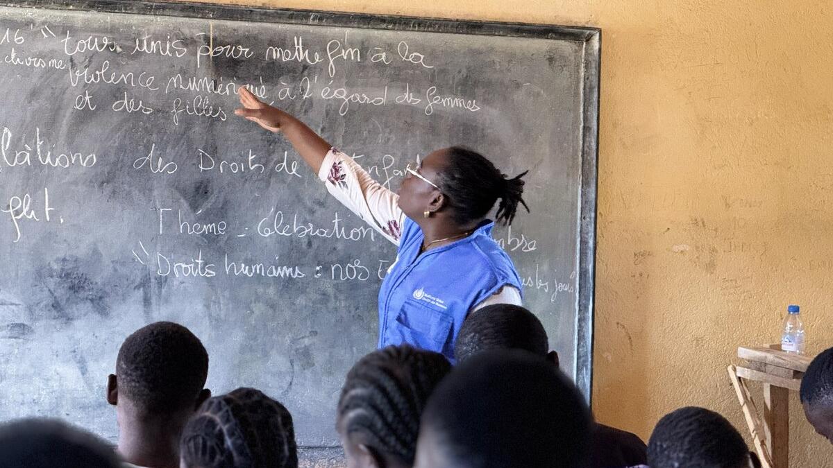 Une femme se tient devant un tableau noir, face à un groupe d'étudiants.