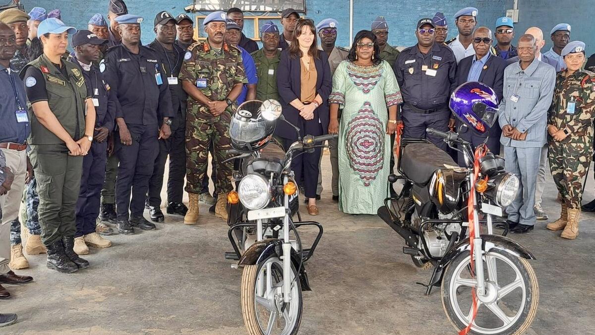 Un groupe de militaires et de civils servant la paix se tient derrière deux motos.