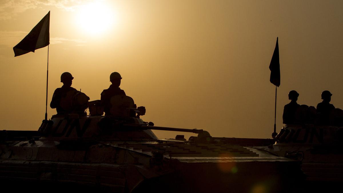 Peacekeepers in their vehicles are silhouetted against the sunset and an orange sky