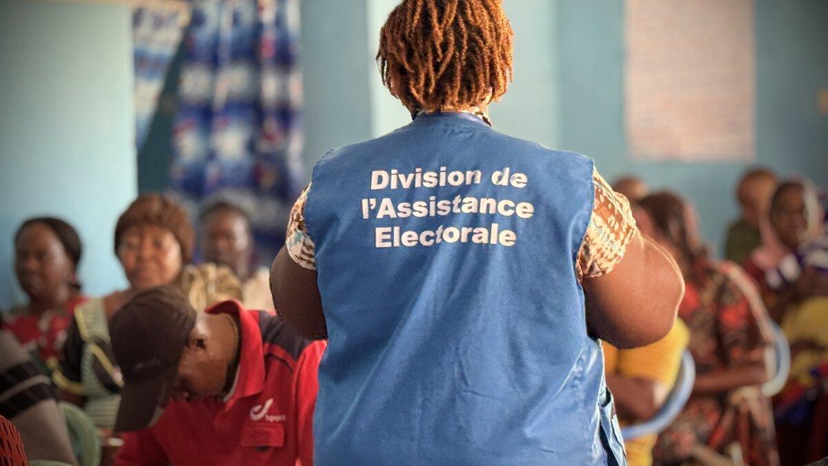 Un représentant porte une veste avec les mots « Division de l’Assistance Électorale ». 