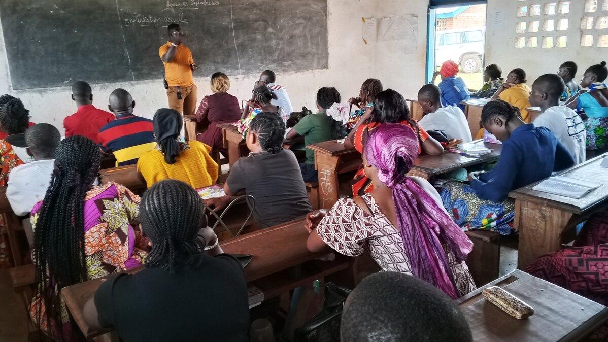 Une salle de classe remplie de gens fait face à une personne debout devant un tableau noir.