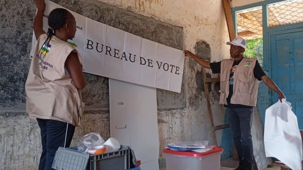 Deux ouvriers assemblent un panneau « Bureau de Vote ».