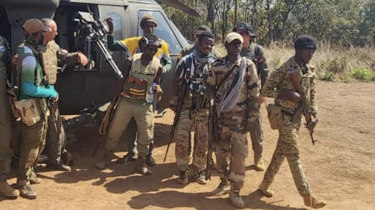 Un groupe de représentants armés se tient à côté d'un hélicoptère.