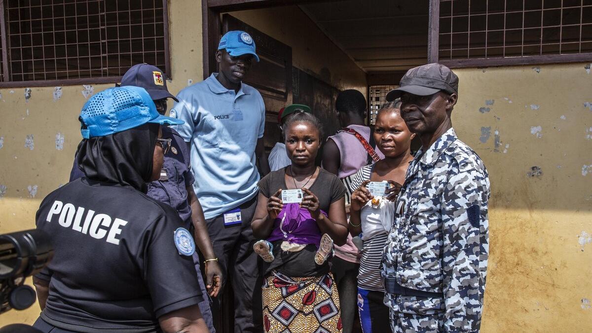 Un électeur tient sa carte d’identité et se tient parmi des représentants de la police.