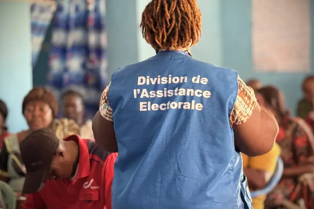 Un représentant porte une veste avec les mots « Division de l’Assistance Électorale ». 