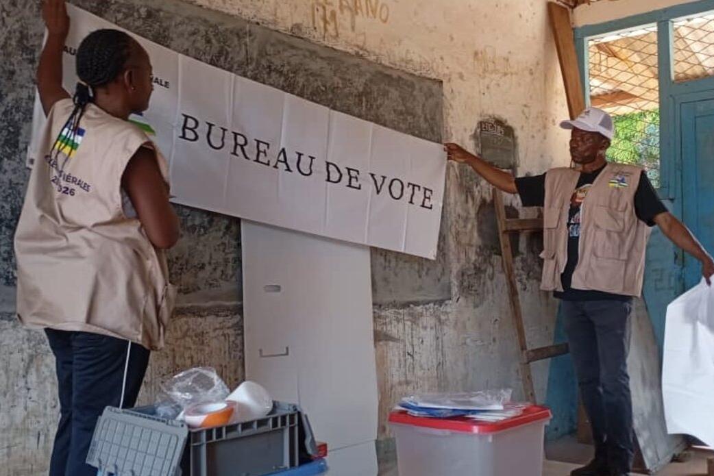 Deux ouvriers assemblent un panneau « Bureau de Vote ».