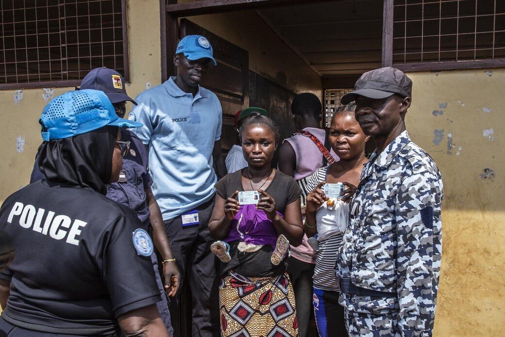 Un électeur tient sa carte d’identité et se tient parmi des représentants de la police.