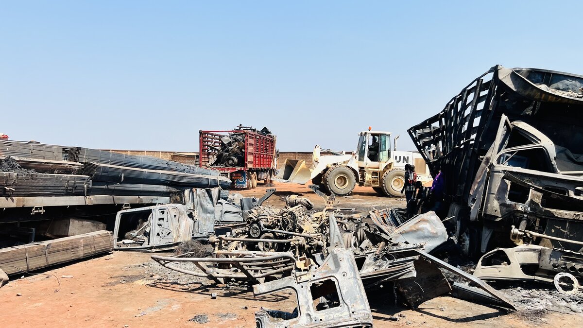 A UN loader (machinery) cleaning debris from burnt trucks and metallic goods.
