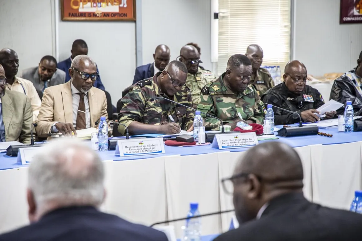 Un groupe de fonctionnaires masculins, en tenue militaire et civile, sont assis à une table avec des microphones.