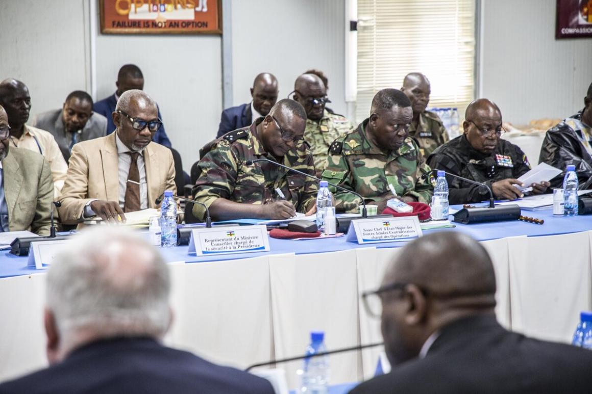 Un groupe de fonctionnaires masculins, en tenue militaire et civile, sont assis à une table avec des microphones.