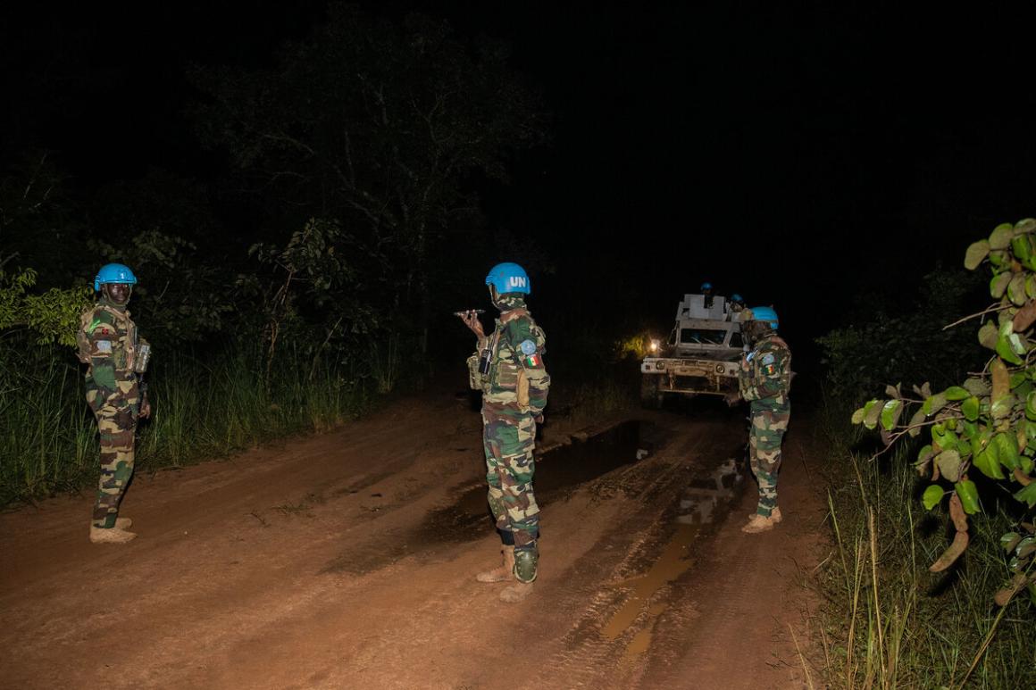 Trois Casques bleus se tiennent devant leur véhicule blindé de transport de troupes la nuit