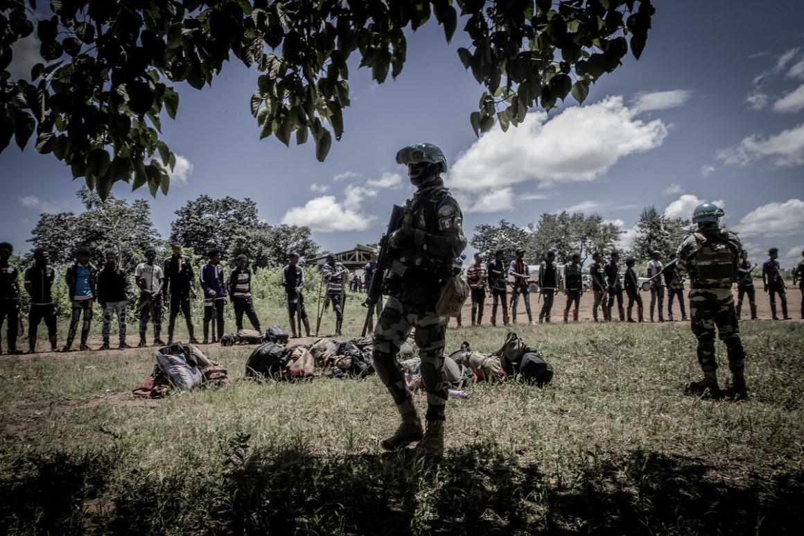 Des Casques bleus armés se tiennent en rang serré à l'extérieur, l'un d'eux se trouvant au premier plan, dans l'ombre.