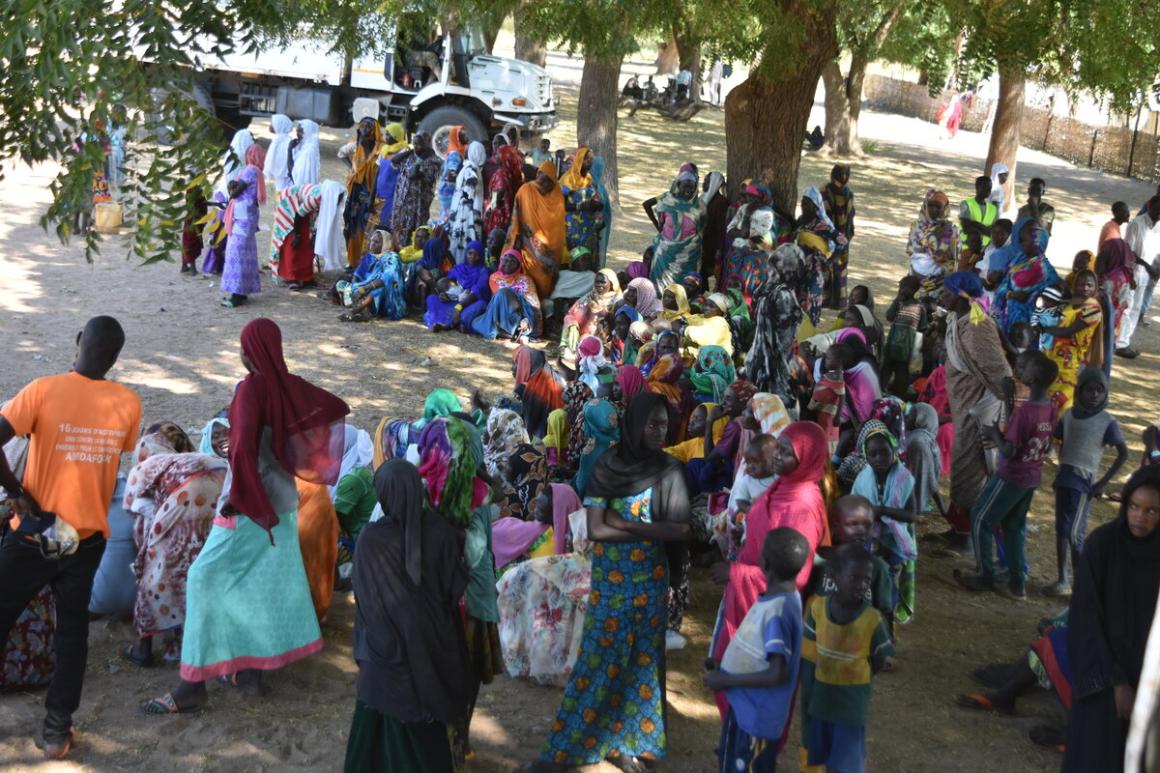 Un grand groupe de personnes se tient en file indienne sous des arbres.