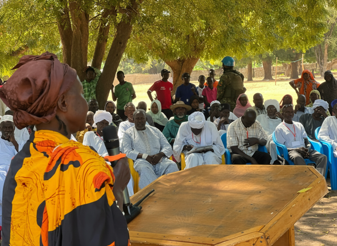 A woman speaks into a microphone in front of a group of community members outside