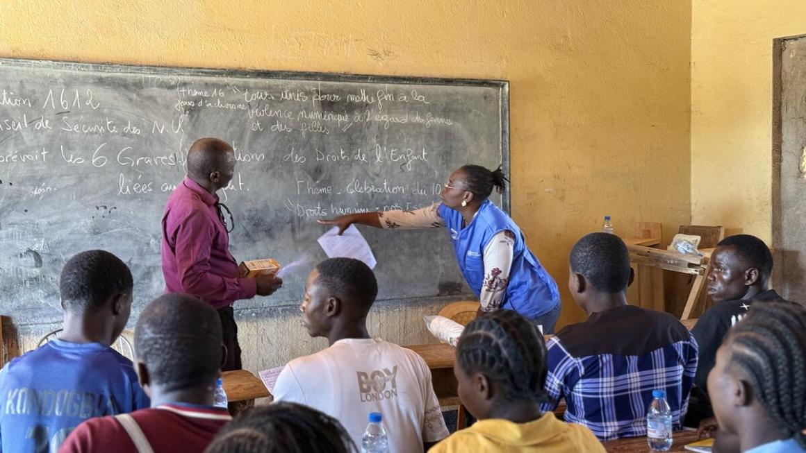 Un homme et une femme se tiennent devant un tableau noir, face à un groupe d'étudiants.