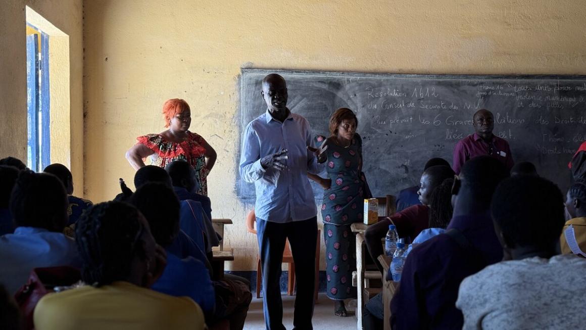 Un groupe de personnes se tient devant un tableau noir, face à un groupe d'élèves.