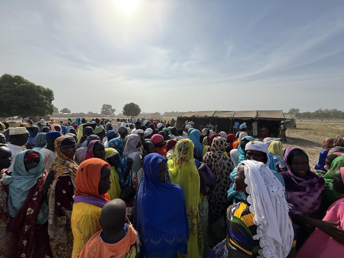 Un grand groupe de personnes se tient dehors sous un ciel bleu ensoleillé.