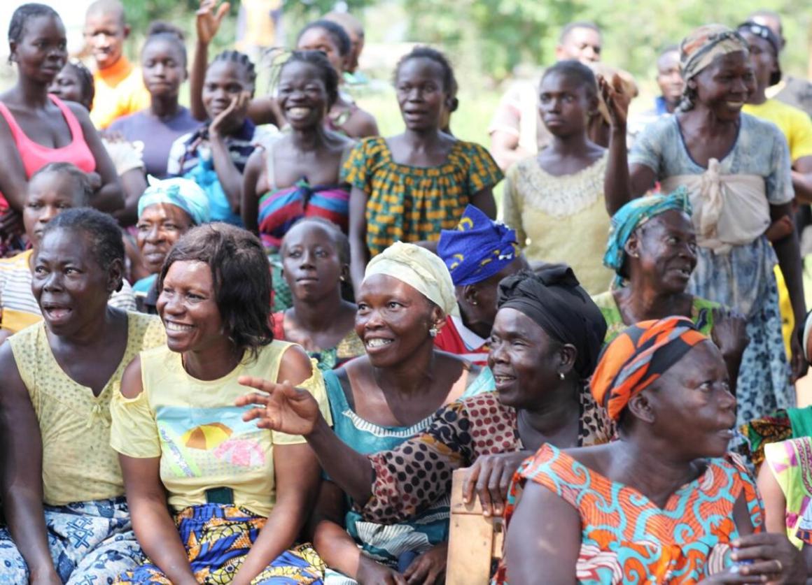 Un groupe de femmes sont assises dehors, souriantes et levant les mains.