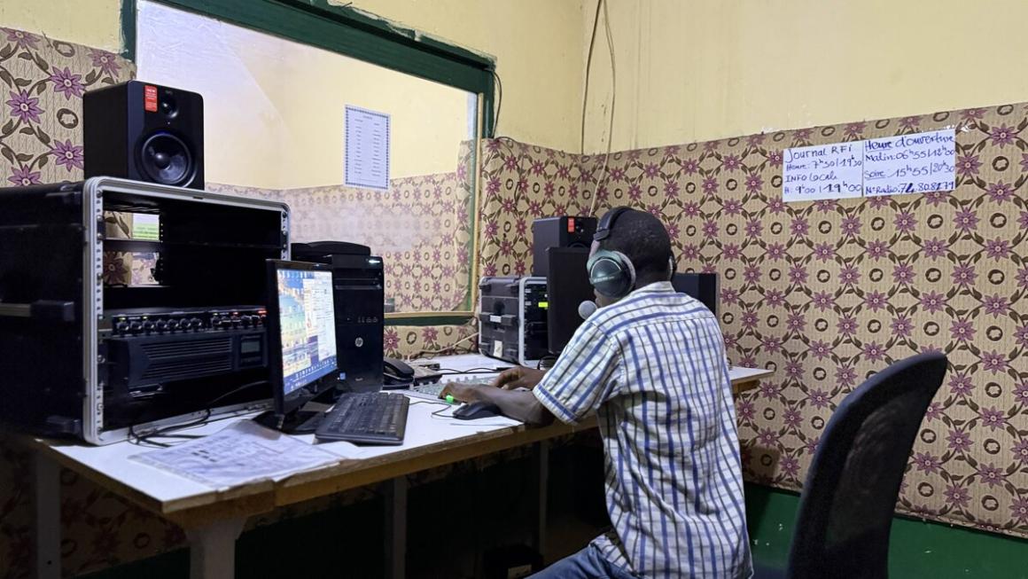 Un homme portant un casque audio est assis devant un ordinateur et d'autres équipements.